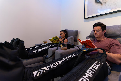 normatec recovery boots in use by two patients in couch while reading