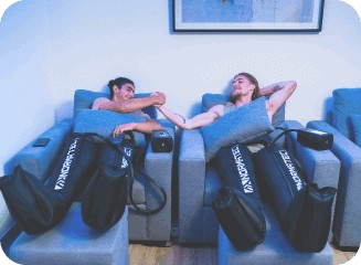 two guys fist bumping while doing normatec boots treatment